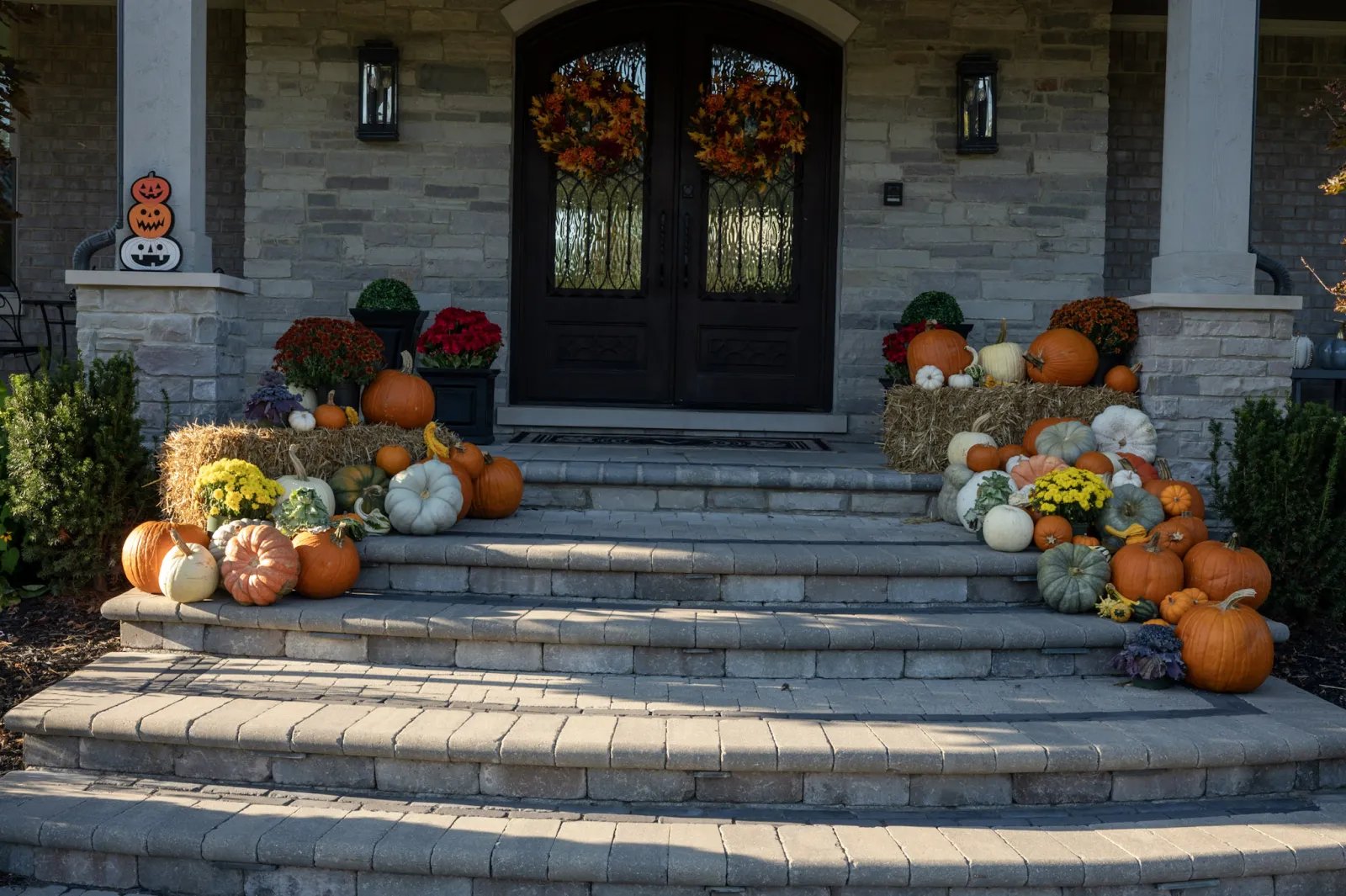 Grand harvest pumpkin display with hay bales and fall wreaths on stone estate porch in Oakland Township MI