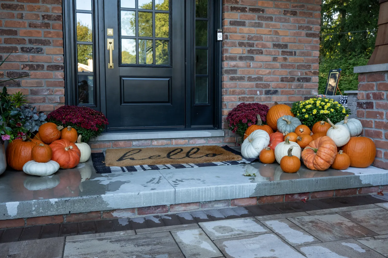 Fall pumpkin porch display with mums and hello doormat on brick home in Beverly Hills MI