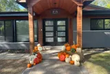Fall front entry with layered orange, white, and heirloom pumpkins and hay bales on a paver walkway at a cedar-entry modern home, professionally designed and installed by Detroit Pumpkin Company in Metro Detroit